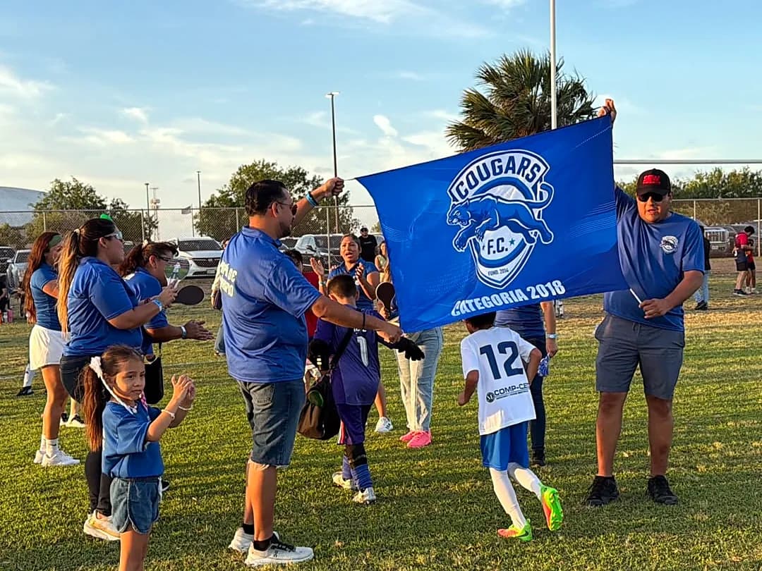 Un papá ondea la bandera de Cougars FC mientras los niños corren alrededor